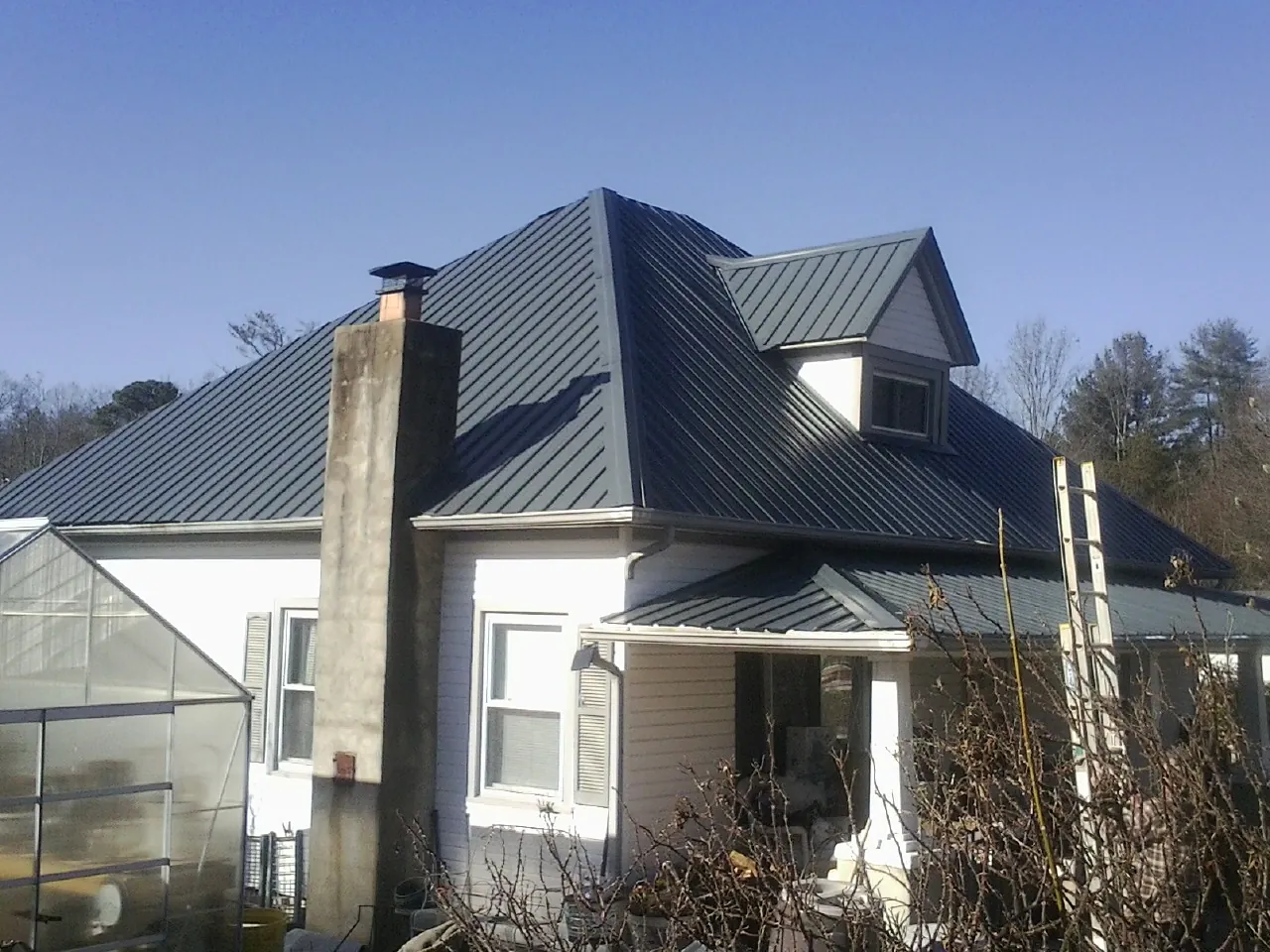 Dark blue standing seam metal roof on a white farmhouse with dormer — Slate & Tile Roof Repair by Roofing Brothers in Little Rock