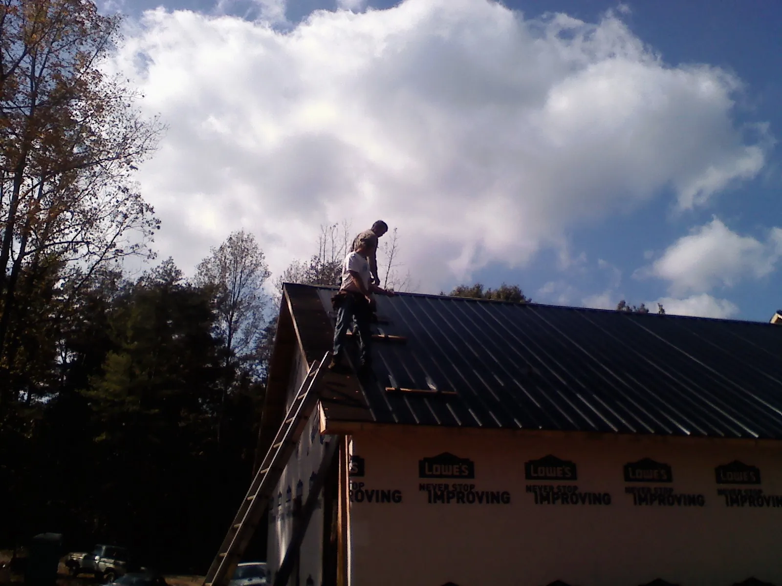 Roofer fastening dark metal panels high against a cloudy sky, from a Roof Inspection job in Little Rock
